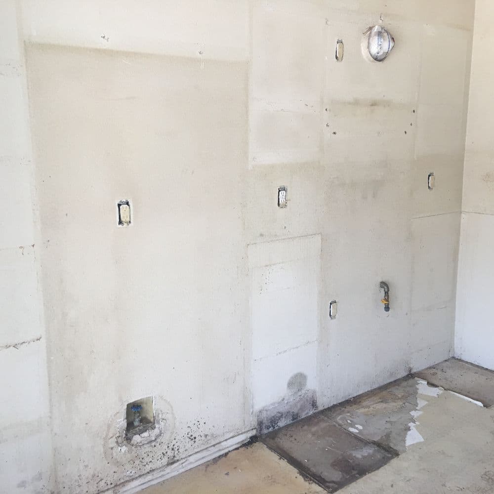 Bare, unfinished wall with exposed electrical boxes and moisture stains in a construction area.