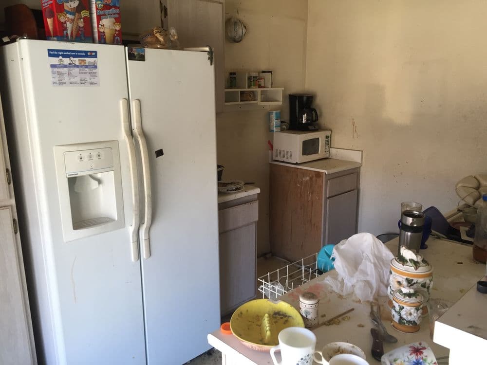 Cluttered kitchen with dirty dishes, a white refrigerator, and various appliances visible.