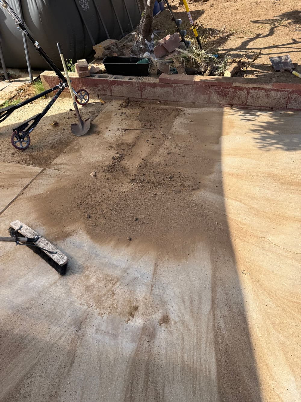 Construction site with sandy ground, tools, and a shaded area, ready for landscaping work.